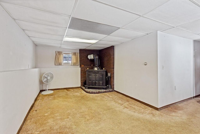 basement featuring a paneled ceiling, a wood stove, baseboards, and carpet floors