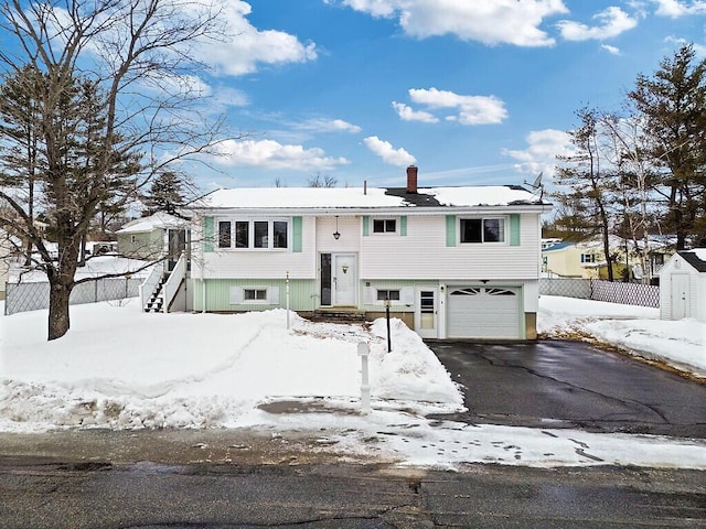 raised ranch featuring aphalt driveway, fence, a chimney, and a garage