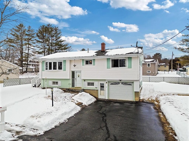 split foyer home featuring driveway, entry steps, a chimney, an attached garage, and fence