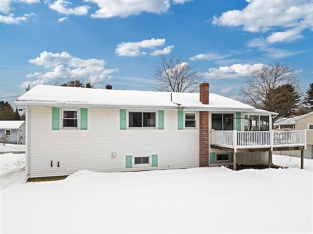 snow covered rear of property featuring a sunroom and a chimney