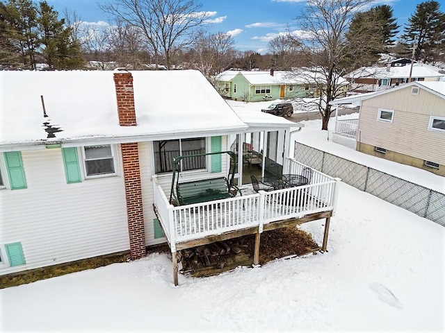 snow covered property with fence, a chimney, and a wooden deck