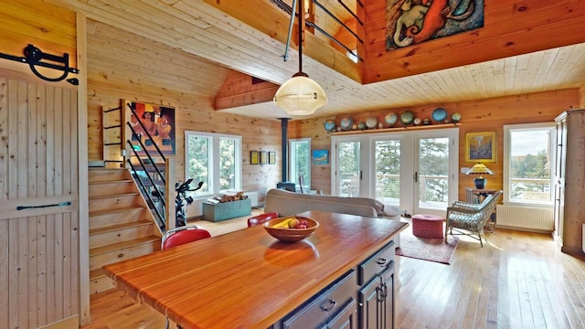 dining room with light wood finished floors, stairway, a wood stove, wood walls, and wooden ceiling