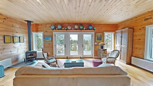 living room with radiator, light wood-style flooring, radiator heating unit, a wood stove, and wooden ceiling