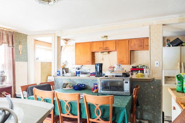 kitchen featuring white refrigerator with ice dispenser, brown cabinetry, and a toaster