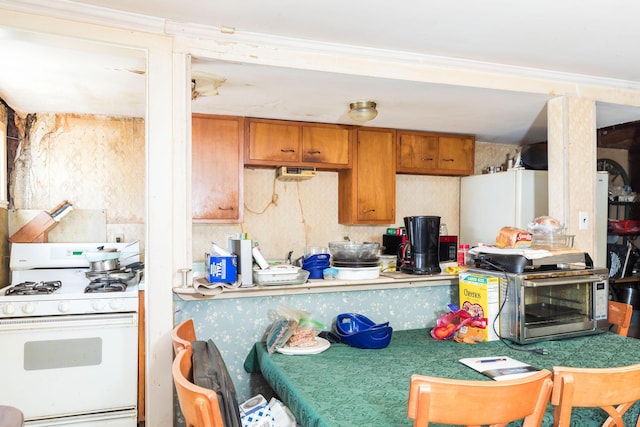 kitchen featuring ornamental molding, a toaster, brown cabinets, and white gas range oven