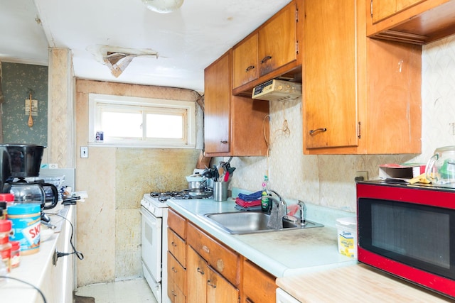 kitchen featuring white range with gas cooktop, brown cabinets, light countertops, under cabinet range hood, and a sink