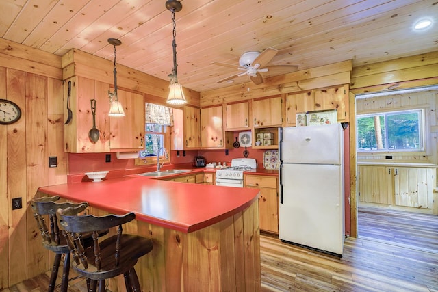 kitchen featuring wooden walls, a peninsula, light wood-style floors, white appliances, and a sink