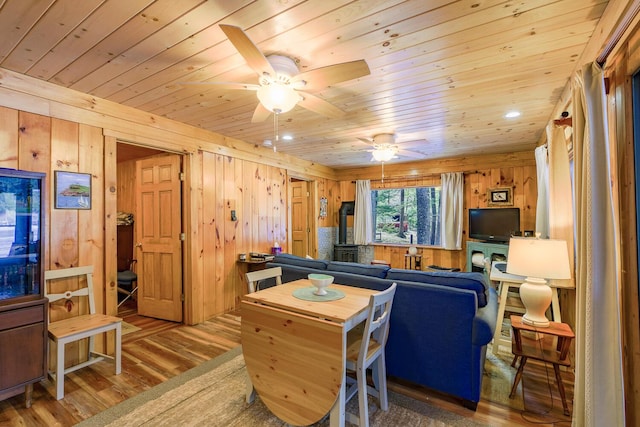 living area featuring wooden walls, wooden ceiling, a wood stove, wood finished floors, and a ceiling fan