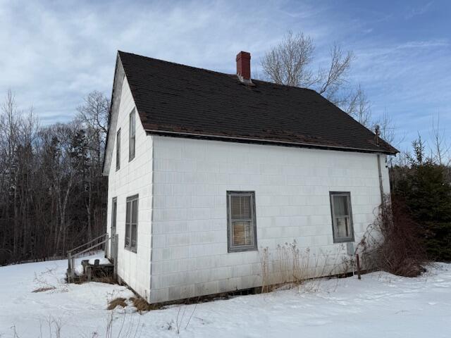 snow covered property with a chimney, concrete block siding, and roof with shingles