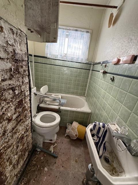 bathroom featuring tiled bath, tile walls, and toilet