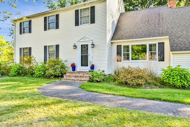 colonial-style house featuring entry steps, a shingled roof, a chimney, and a front yard