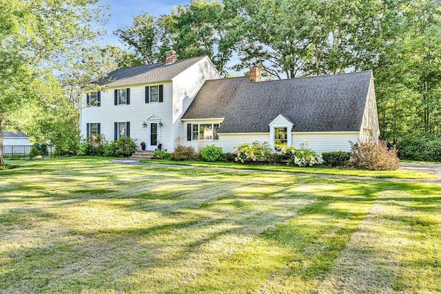 colonial-style house featuring a shingled roof, a chimney, and a front lawn