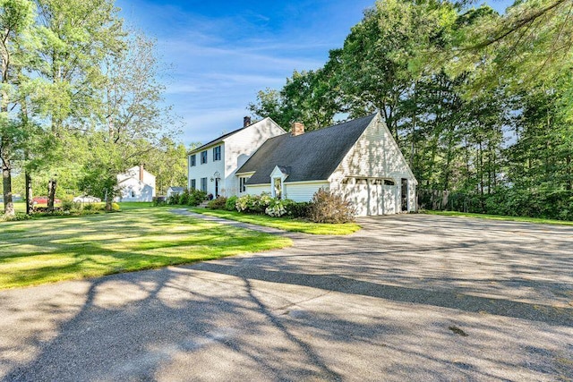 view of side of home featuring a yard, a chimney, an attached garage, and driveway