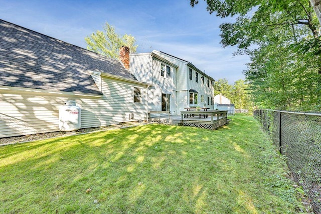 back of property with a deck, a fenced backyard, a shingled roof, a lawn, and a chimney