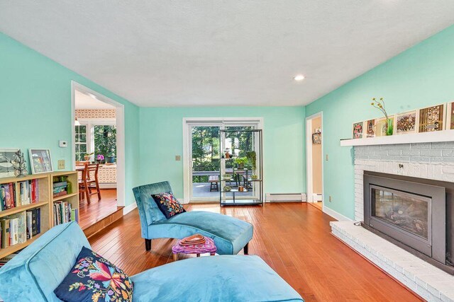 living room with a baseboard radiator, a fireplace, a wealth of natural light, and light wood-style floors