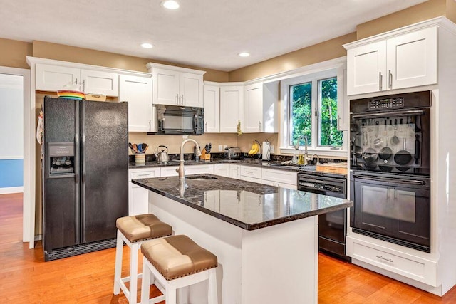 kitchen featuring dark stone counters, a center island, white cabinets, and black appliances