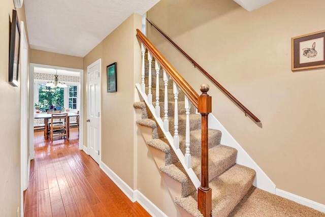 stairs with a notable chandelier, baseboards, and wood finished floors