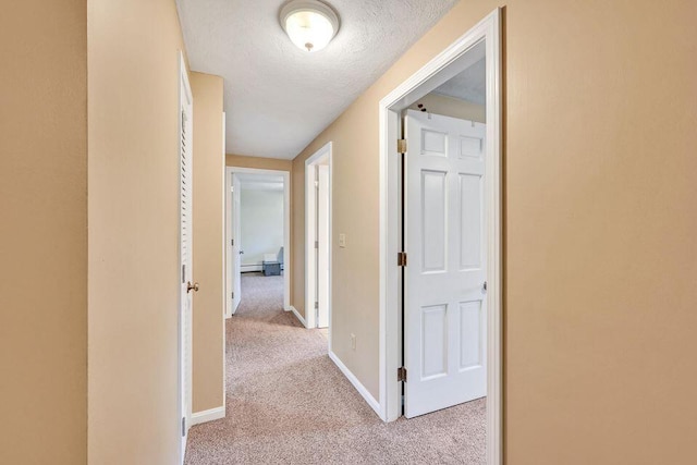 hall featuring light colored carpet, a textured ceiling, and baseboards