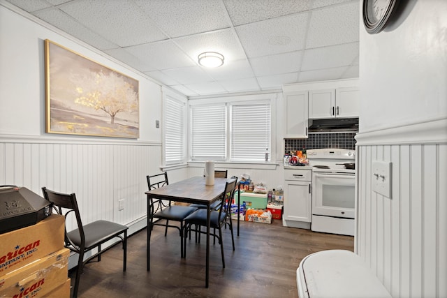 dining room with a drop ceiling, a wainscoted wall, and dark wood-style flooring