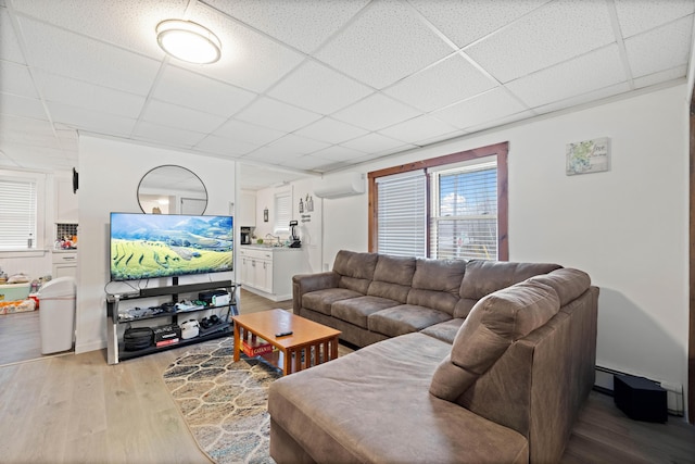 living area with a drop ceiling, light wood-style flooring, and a wall mounted AC