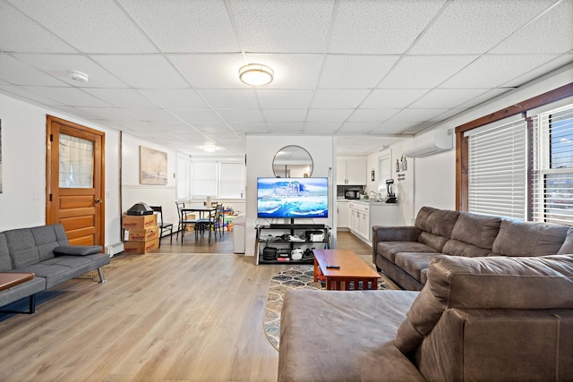 living room with a wall unit AC, a paneled ceiling, light wood-type flooring, and baseboard heating