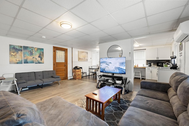 living room featuring a paneled ceiling, light wood finished floors, and a wall mounted AC