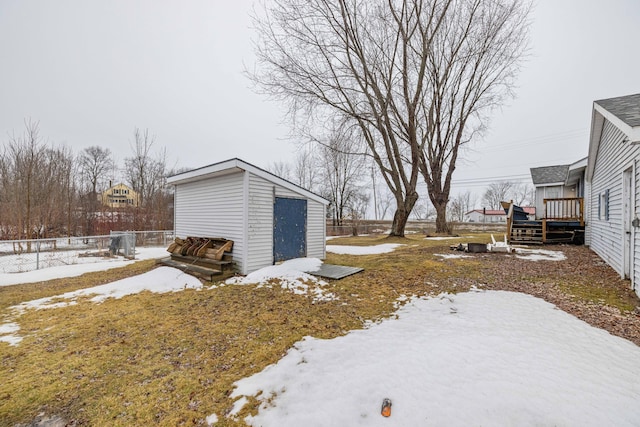 yard layered in snow featuring an outbuilding, a deck, a storage shed, and fence