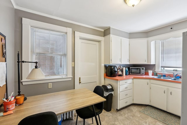 kitchen featuring a toaster, ornamental molding, light countertops, white cabinetry, and a sink