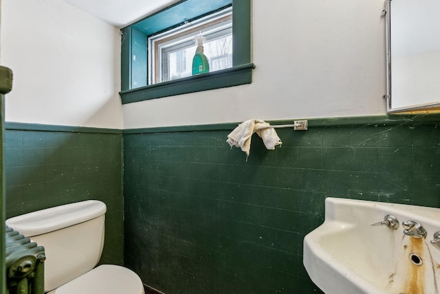 bathroom with a wainscoted wall, a sink, tile walls, and toilet