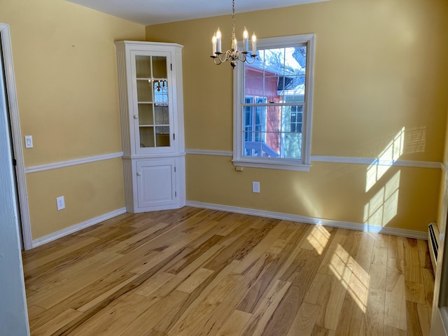 unfurnished dining area with baseboards, light wood finished floors, and a notable chandelier