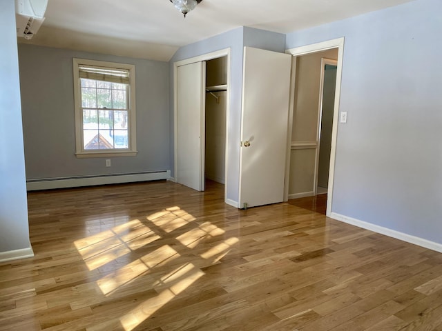 unfurnished bedroom featuring lofted ceiling, a closet, a baseboard heating unit, light wood-style floors, and baseboards