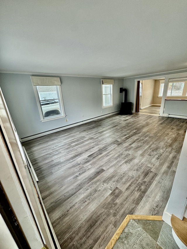 unfurnished living room with a wood stove, crown molding, baseboards, and wood finished floors