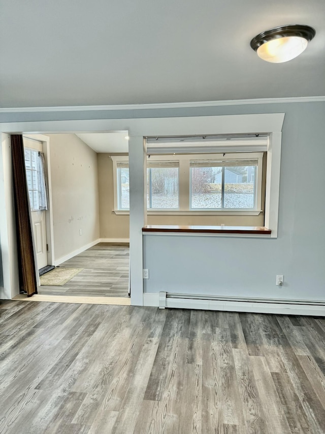 empty room featuring ornamental molding, baseboards, baseboard heating, and wood finished floors