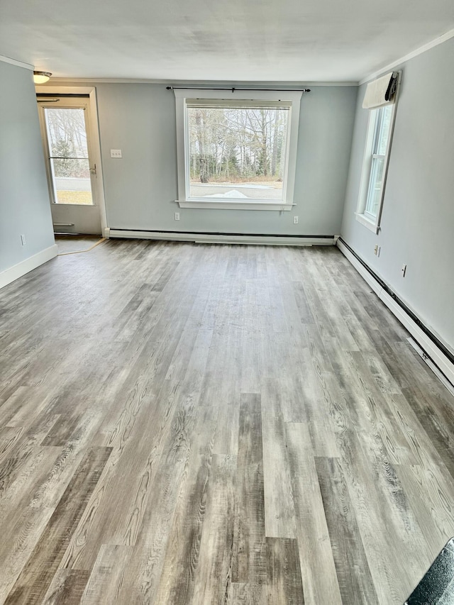 empty room featuring baseboards, baseboard heating, wood finished floors, and crown molding