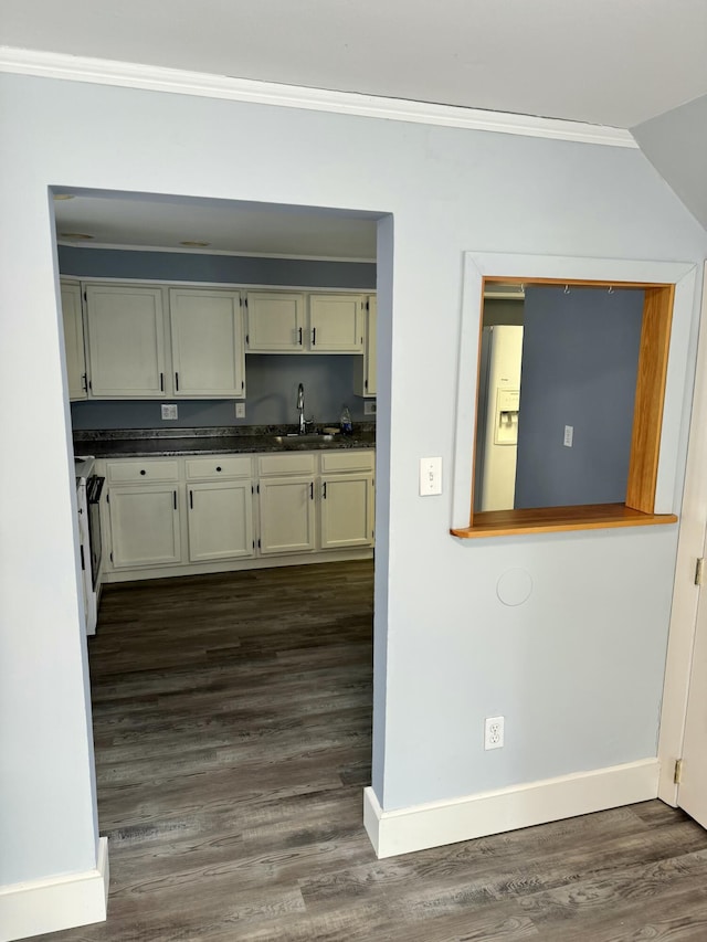 kitchen featuring white refrigerator with ice dispenser, a sink, baseboards, dark wood-style floors, and dark countertops