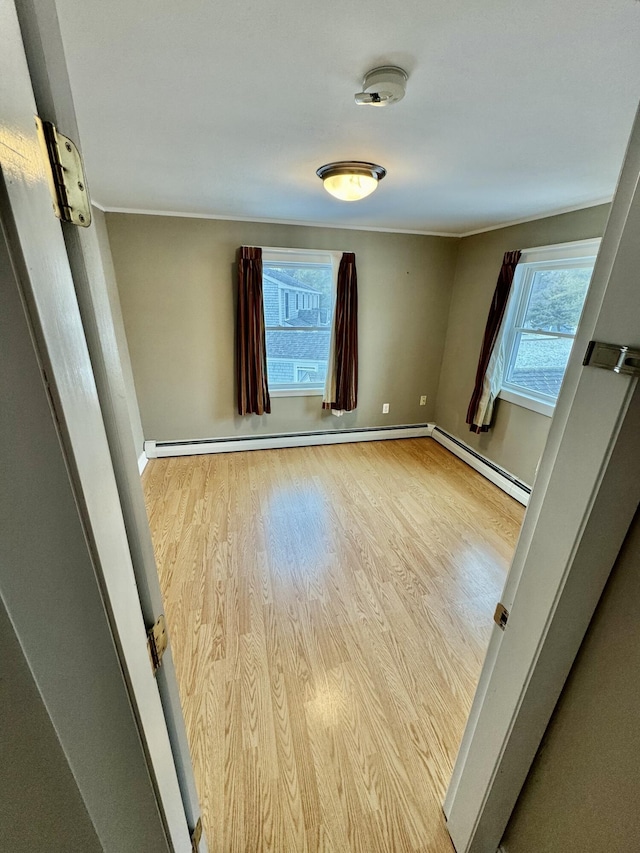 unfurnished room featuring baseboard heating, wood finished floors, and baseboards