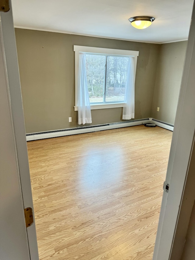 spare room featuring a baseboard heating unit and light wood finished floors