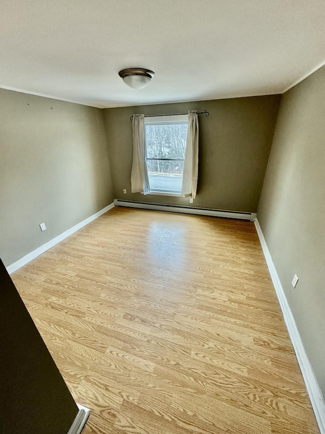 unfurnished room featuring a baseboard heating unit, wood finished floors, and baseboards