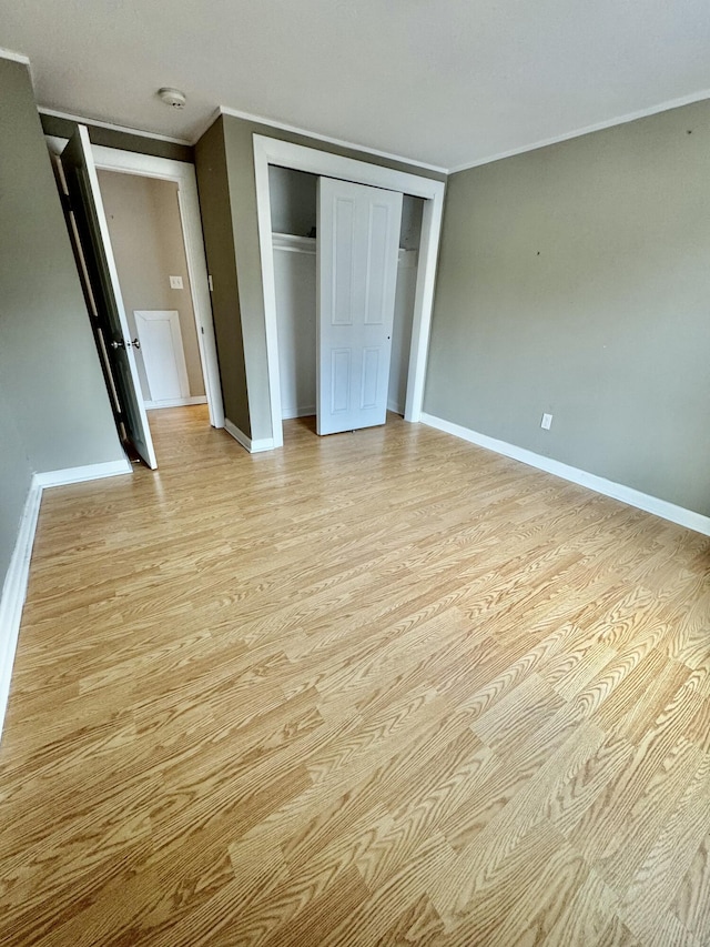 unfurnished bedroom featuring ornamental molding, a closet, light wood-style flooring, and baseboards