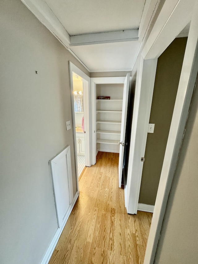 hallway featuring built in shelves, light wood-style flooring, and baseboards