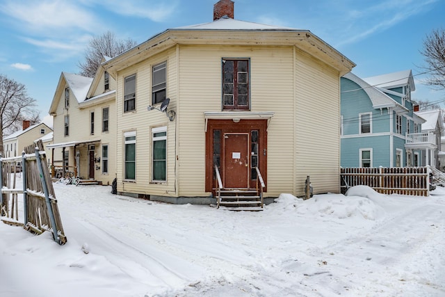 view of front of home with entry steps, a chimney, and fence