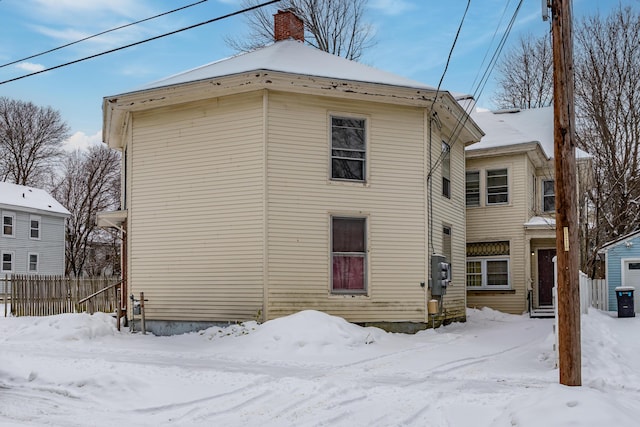 snow covered back of property with a chimney and fence