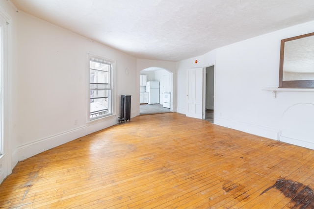 unfurnished living room featuring arched walkways, baseboards, and light wood-style floors