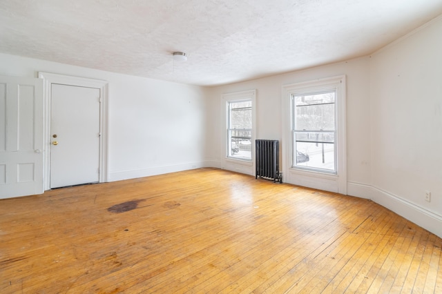 unfurnished living room with radiator heating unit, baseboards, light wood-style flooring, and a textured ceiling