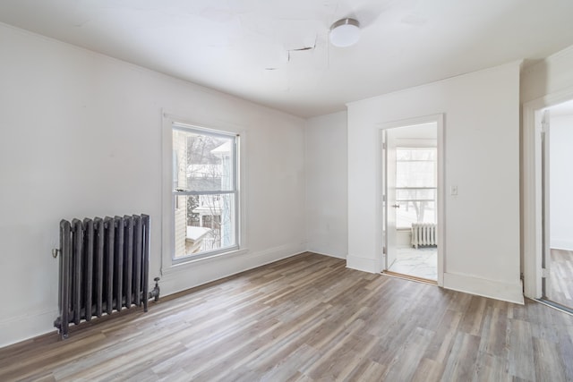 empty room with radiator, light wood-style flooring, and baseboards