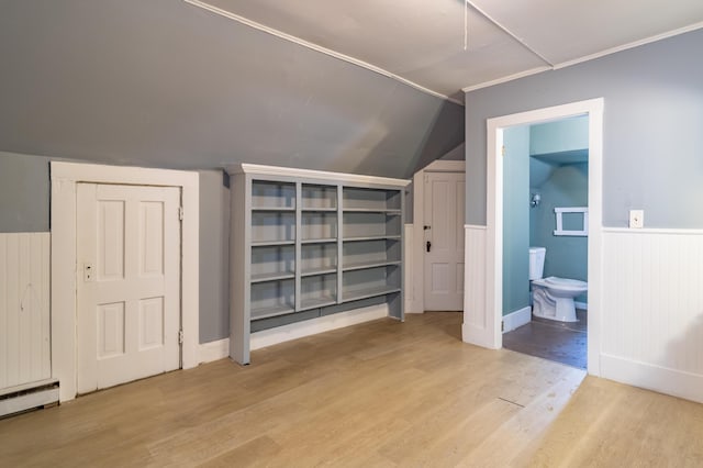 additional living space featuring a wainscoted wall, vaulted ceiling, a baseboard radiator, and light wood-style flooring