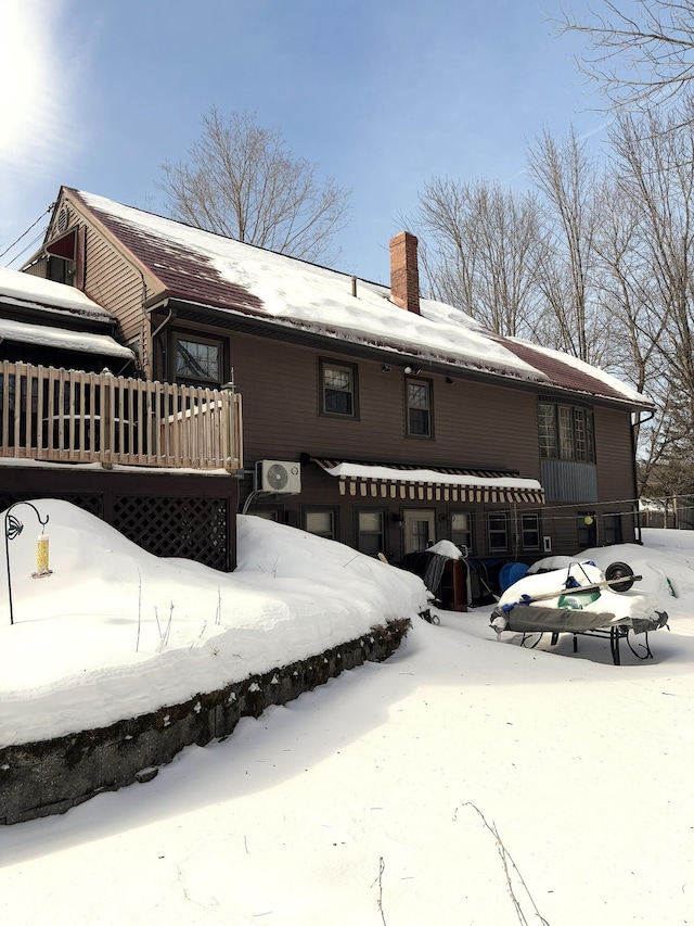 snow covered rear of property with a deck and a chimney