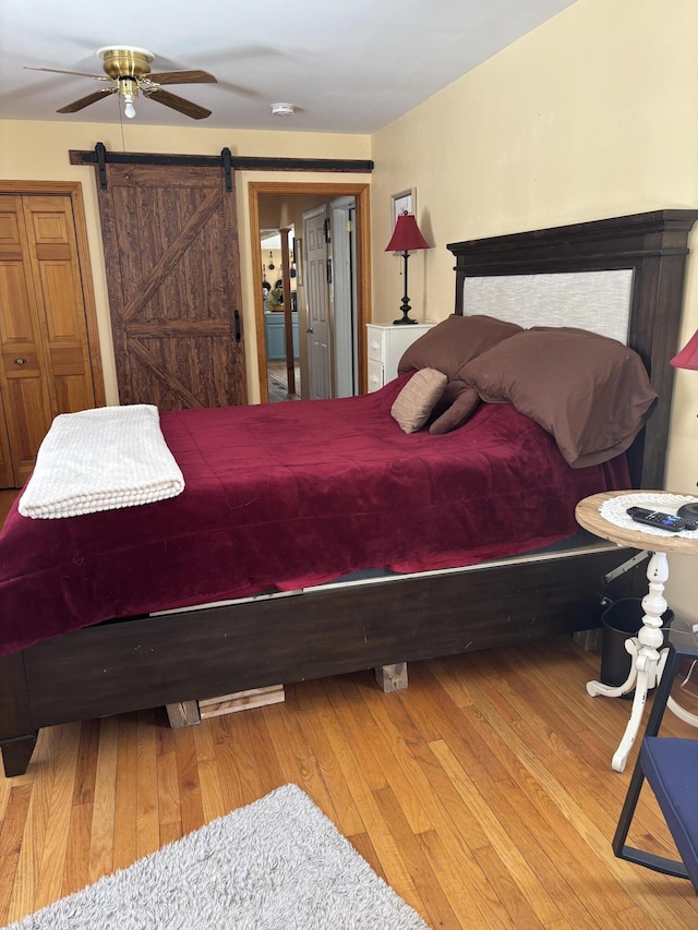 bedroom with ceiling fan, light wood finished floors, and a barn door