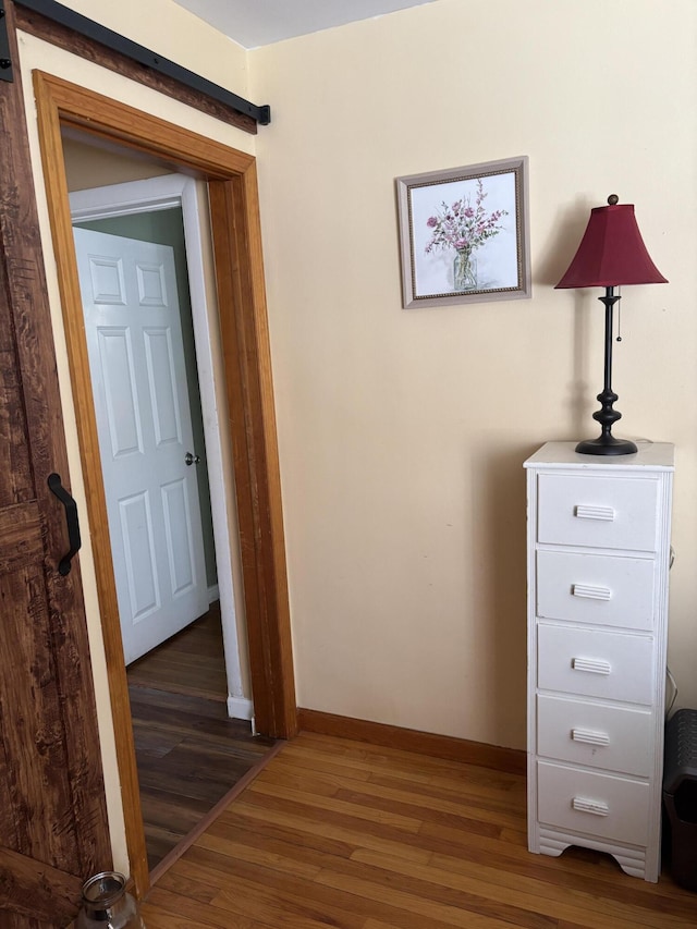 corridor with a barn door, dark wood-type flooring, and baseboards