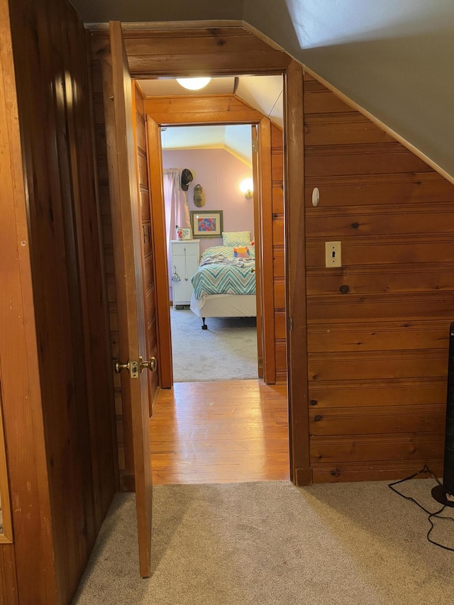 hall with light wood-type flooring, vaulted ceiling, light colored carpet, and wood walls